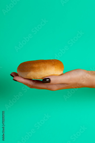 Female hand holding a hamburger bun on green background..