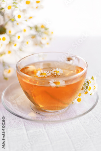  cup of herbal chamomile tea, on a cozy light background with fresh chamomile flowers 