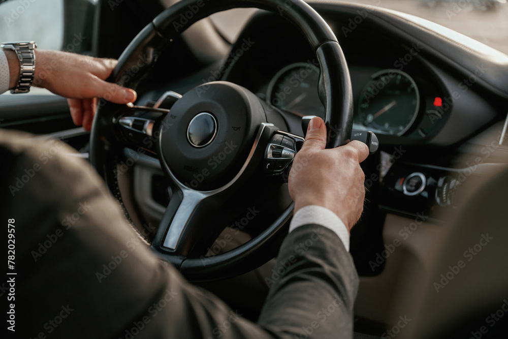 Close up view of steering wheel. Man in black suit is sitting in the car, driving