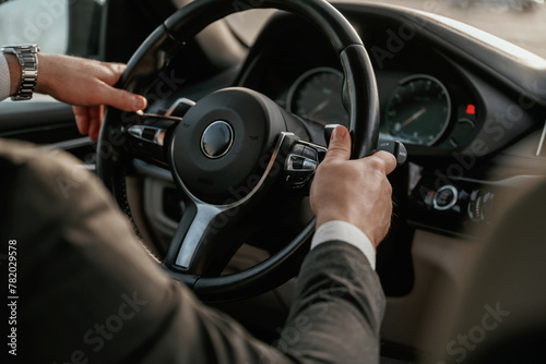 Close up view of steering wheel. Man in black suit is sitting in the car, driving
