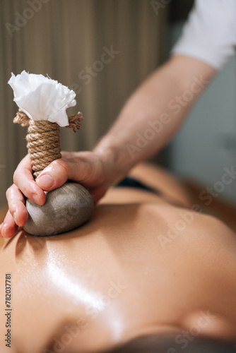 Cropped vertical shot of Ayurveda Massage therapist pressing herbal bolus bags onto female skin. Masseur gently compresses herb bag on woman body. Hot herbal ball spa massage body treatment.