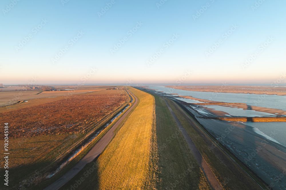 Fototapeta premium Embankment protecting residents in the southern Netherlands from ocean water under a brilliant orange-yellow sunrise. Breathtaking morning