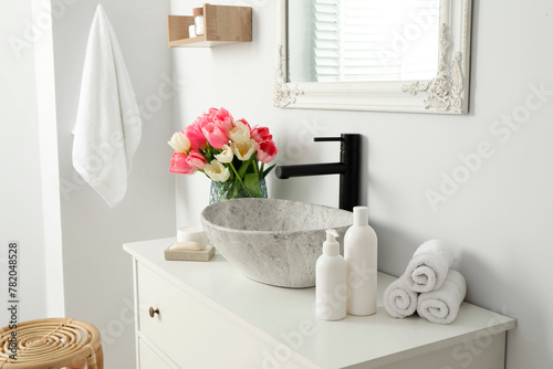 Vase with beautiful pink tulips and toiletries near sink in bathroom