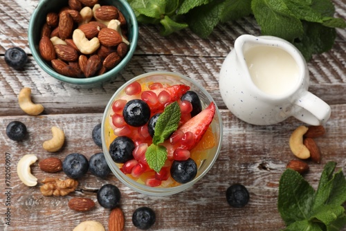 Delicious fruit salad, fresh berries, mint and nuts on wooden table, flat lay