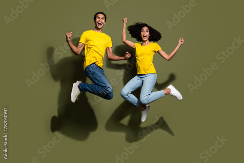 Full size photo of two young people jump raise fists wear t-shirt isolated on khaki color background