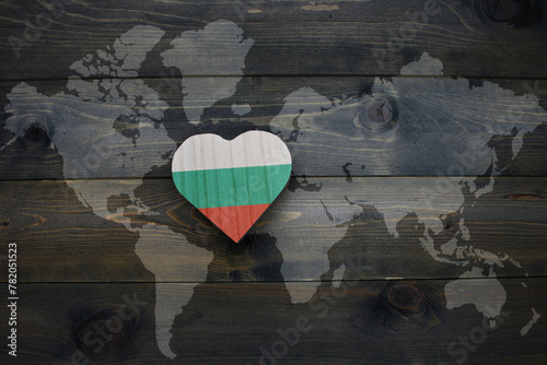 wooden heart with national flag of bulgaria near world map on the wooden background.