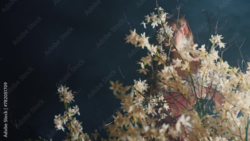 fantasy woman walking through branches in saint divine light ray in black night dark forest glow fog tree white flowers blooming tree. sexy lady fairy elf Girl blond fashion model. magic smoke art 4k