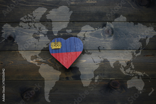 wooden heart with national flag of liechtenstein near world map on the wooden background.