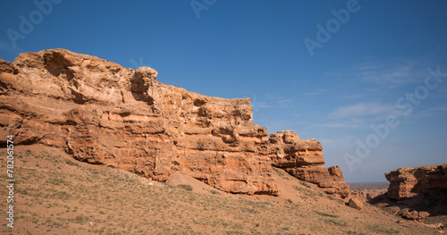 large rock formation against a deep blue sky. The rock s surface is rugged and pitted  with shades of brown that suggest erosion from environmental elements.