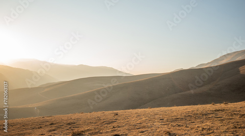 Early morning sunlight bathes gentle hills and valleys with a soft, hazy light, emphasizing the tranquil beauty of this vast, open landscape.