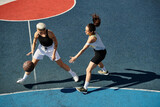 Two athletic young women stand triumphantly atop a basketball court in the summer sun.