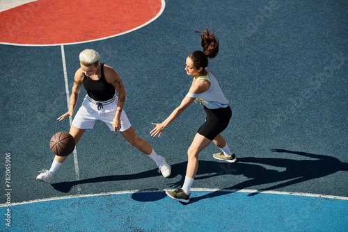 Two athletic young women stand triumphantly atop a basketball court in the summer sun. © LIGHTFIELD STUDIOS