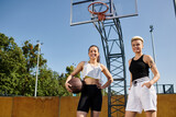 Two young athletic women playing basketball by a hoop outdoors on a sunny day.