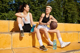 Athletic female friends, young women playing basketball outdoors, enjoying a relaxing moment together.