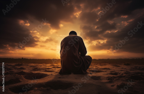 Prayer concept. Silhouette of a young man in a praying pose. Set against a vibrant sunset sunrise sky. Clasped hands. Also related to gospel, testimony, deliverance, providence, mercy