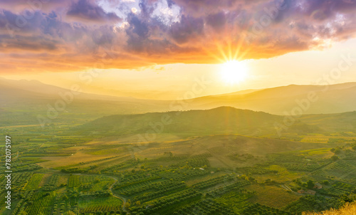 scenic rustic landscape with green hills and farms in a mountain valley during colorful cloudy sunset