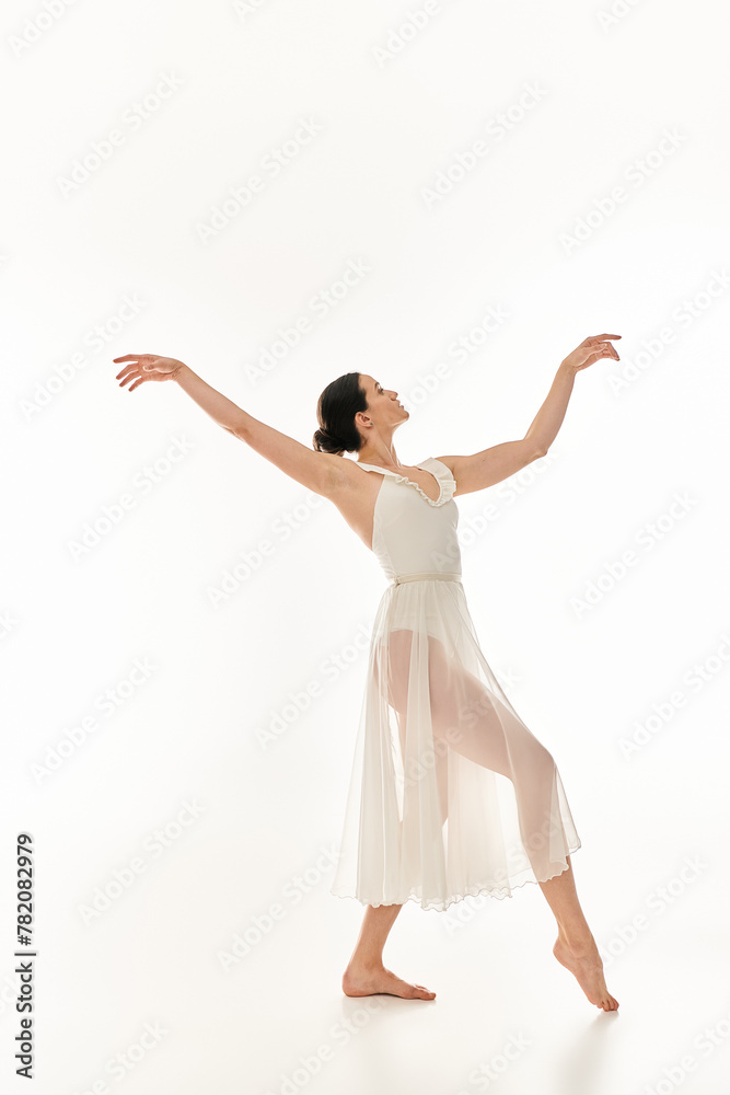 A graceful young woman dances in a flowing white dress against a white studio backdrop.