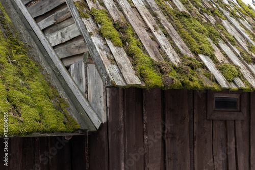 Old wooden house exterior details. Roof with green moss and walls