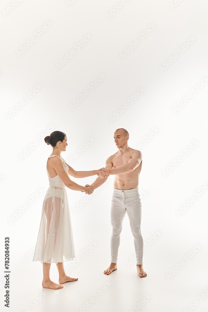 A shirtless young man and a young woman in a white dress perform acrobatic elements as they hold hands in front of a white background. A shirtless young man and a young woman in a white dress perform acrobatic elements as they hold hands in front of a white background.