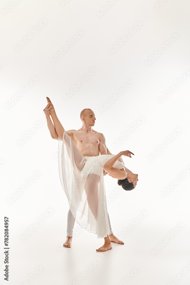 A shirtless young man and a woman in a white dress performing acrobatic dance moves together in a studio setting against a white backdrop. A shirtless young man and a woman in a white dress performing acrobatic dance moves together in a studio setting against a white backdrop.