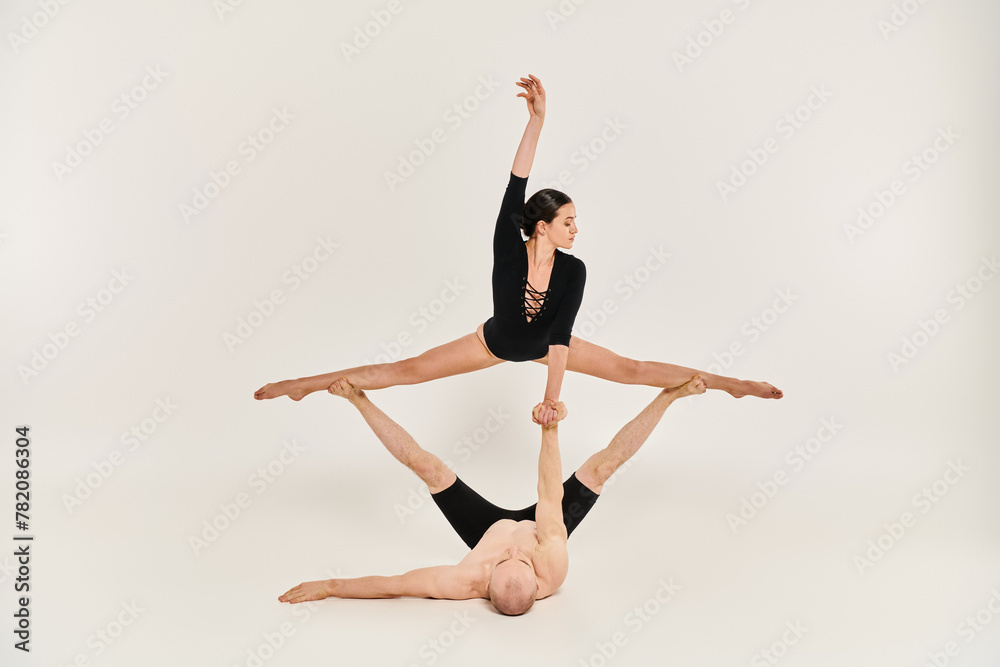 A shirtless young man and a woman gracefully perform acrobatic moves while suspended in the air in a studio setting.