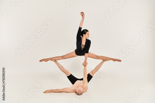 A shirtless young man and a woman gracefully perform acrobatic moves while suspended in the air in a studio setting.