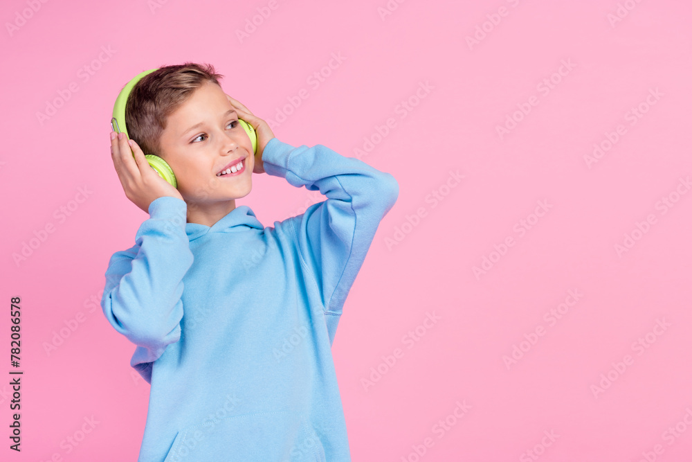Photo of positive little boy arms touch headphones look empty space imagine isolated on pink color background Photo of positive little boy arms touch headphones look empty space imagine isolated on pink color background