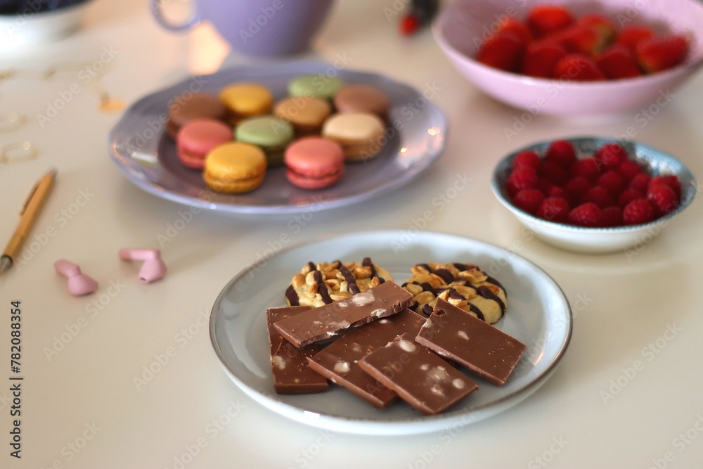 Plate of pastel macarons, cookies and chocolate, cup of tea of coffee, glass of bubble water, various berries, books and accessories on the table. Selective focus, pastel colors. Plate of pastel macarons, cookies and chocolate, cup of tea of coffee, glass of bubble water, various berries, books and accessories on the table. Selective focus, pastel colors.