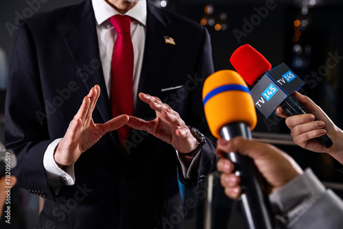 Serious male American politician talks with journalists, answers questions and gives interview for media and television news in government building. United States congressman during press conference.