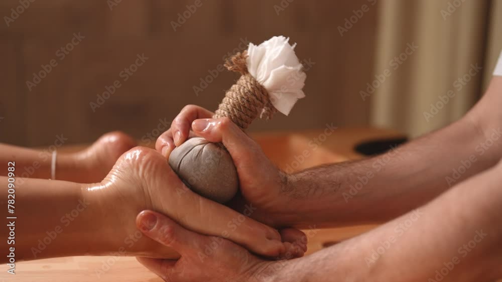 Closeup of unrecognizable relaxed woman getting Ayurvedic feet massage with Kizhi Herbal Bags by male masseur in luxury resort spa salon for body relaxation and skin care. Shooting in slow motion