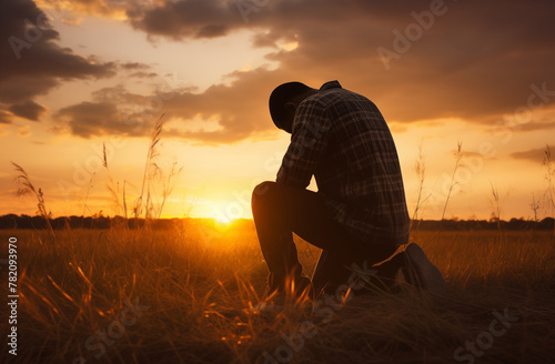 Prayer concept. Silhouette of a young man in a praying pose. On his Knees. Set against a vibrant sunset sunrise sky. Clasped hands. Also related to sacrifice, sanctification, shepherd, trinity, shadow