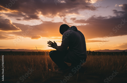 Prayer concept. Silhouette of a handsome black man in a praying pose. Set against a vibrant sunset sunrise sky. Open hands. Also related to faithful, glorify, hallelujah, immanuel, justification