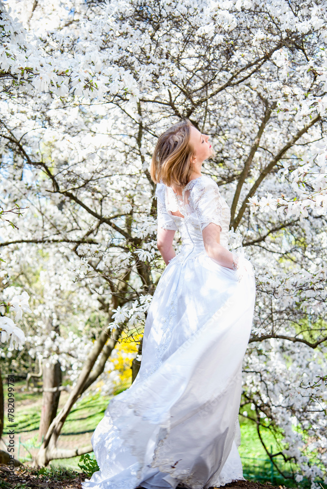beautiful blonde smiling romantic bride in a white dress walking in blossoming magnolia garden on sunny spring day beautiful blonde smiling romantic bride in a white dress walking in blossoming magnolia garden on sunny spring day