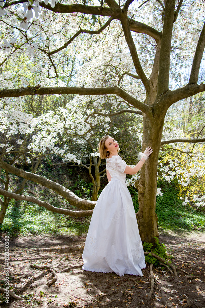 beautiful blonde smiling romantic bride in a white dress walking in blossoming magnolia garden on sunny spring day beautiful blonde smiling romantic bride in a white dress walking in blossoming magnolia garden on sunny spring day