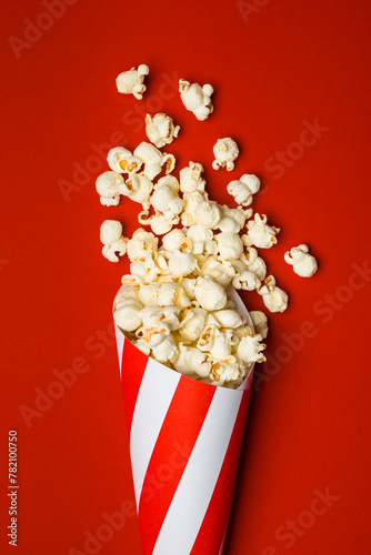 Flat lay composition with popcorn in paper cone on red background.
