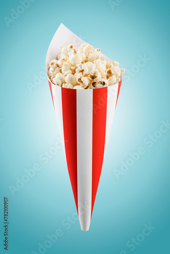 Popcorn in red and white striped paper cone on blue background.