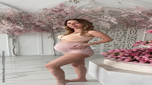 Beautiful pregnant woman in special beige pregnancy underwear. Advertisement of comfortable basic pregnancy underpants. Happy blond girl show her panties in room with flowers. Caucausian woman stand