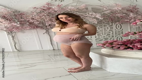 Beautiful pregnant woman in special beige pregnancy underwear. Advertisement of comfortable basic pregnancy underpants. Happy blond girl show her panties in room with flowers. Caucausian woman stand