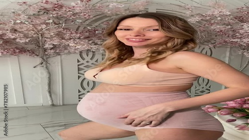 Beautiful pregnant woman in special beige pregnancy underwear. Advertisement of comfortable basic pregnancy underpants. Happy blond girl show her panties in room with flowers. Caucausian woman stand