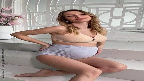 Beautiful pregnant woman in special beige pregnancy underwear. Advertisement of comfortable basic pregnancy underpants. Happy blond girl show her panties in room with flowers. Caucausian woman stand