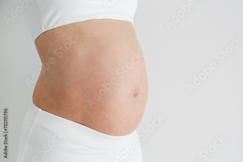 Cropped shot of pregnant woman wearing supportive maternity bra, showing her bare belly. Background, copy space, close up.