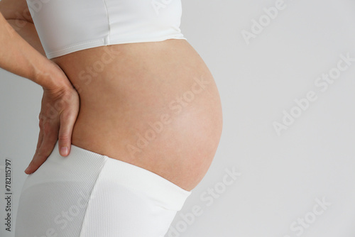 Cropped shot of pregnant woman wearing seamless maternity bra with hands supporting her lower back. Background, copy space, close up.