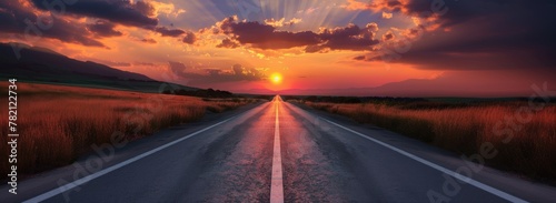 Road stretches towards breathtaking sunset, Straight asphalt road, golden sky above, fluffy clouds, silhouetted mountains evoke tranquil, scenic journey ahead.