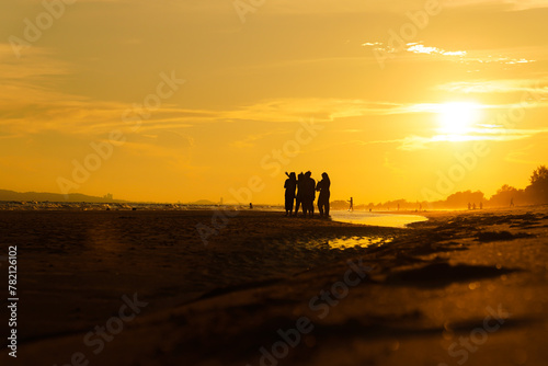 Silhouette of a group of friends enjoying the sunset on the beach at golden sunset time, relaxing on a relaxing vacation, sea in the evening.