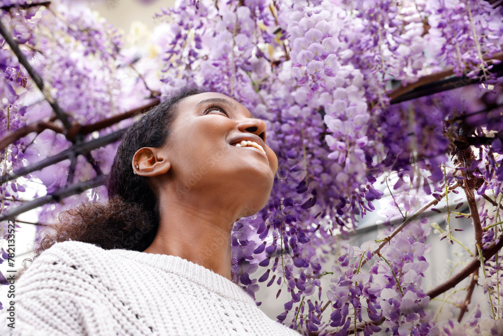 An African American woman is fully surprised with the beauty of the purple wisteria flower in the square metal garden arch An African American woman is fully surprised with the beauty of the purple wisteria flower in the square metal garden arch