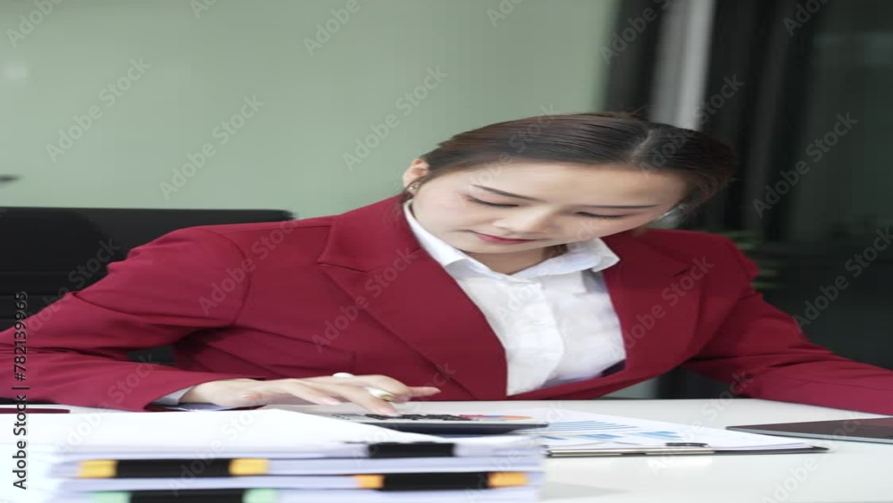 Asian young businesswoman, a Financial Advisor, works happily in her office. She uses her laptop and mobile phone to analyze charts and communicate financial strategies. Red formal suit Asian young businesswoman, a Financial Advisor, works happily in her office. She uses her laptop and mobile phone to analyze charts and communicate financial strategies. Red formal suit