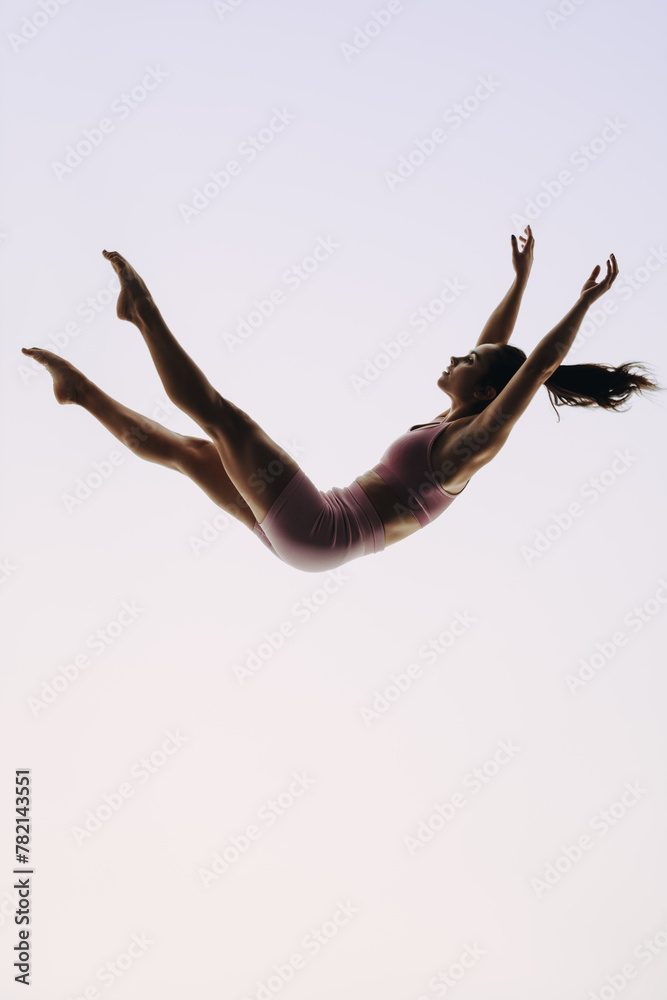 In-flight gymnast: A female acrobatics performer leaps mid-air in a graceful routine - obrazy, fototapety, plakaty 