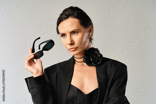 A fashionable woman in a sleek black suit confidently holds up a pair of chic sunglasses, exuding a sense of sophistication and style. © LIGHTFIELD STUDIOS