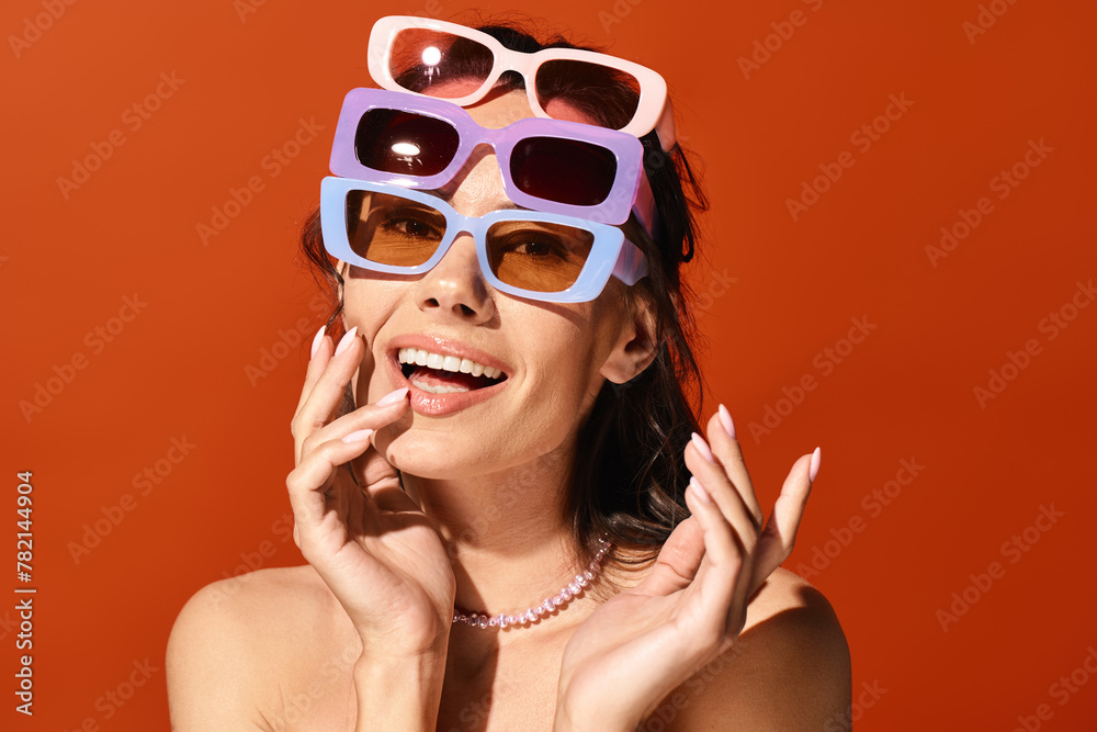 A fashionable woman striking a pose with sunglasses perched atop her head against an orange backdrop. A fashionable woman striking a pose with sunglasses perched atop her head against an orange backdrop.