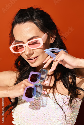 A fashionable woman in a white dress and pink sunglasses posing in a studio on an orange background, exuding summertime style. © LIGHTFIELD STUDIOS
